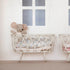 A Maileg stuffed rabbit toy resting on a white Maileg metal cradle against a wall with simple decor.