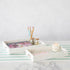 Two Godinger White Marble Rectangular Trays on a striped surface, one holding art supplies and the other candles and a small jar, showcasing the elegance of marble.