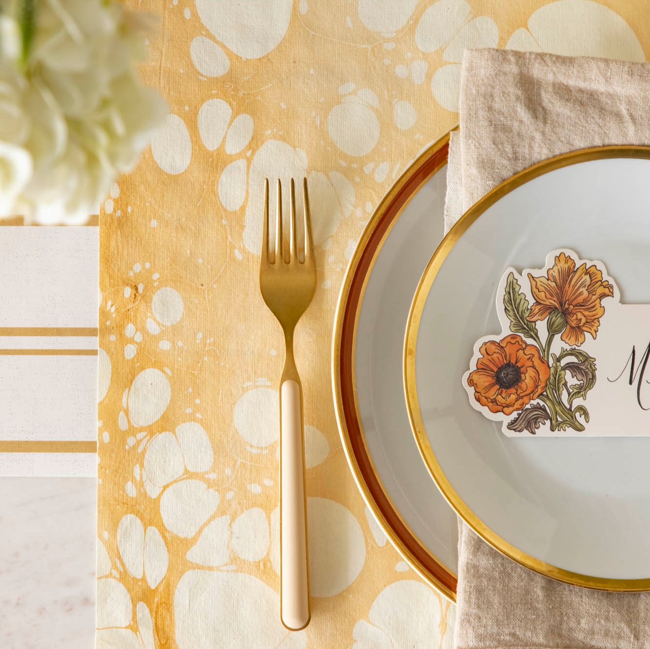 An overhead view of the Gold Stone Marble Placemat with the Antique Gold Stripe runner underneath and a gold and tan fork on top.