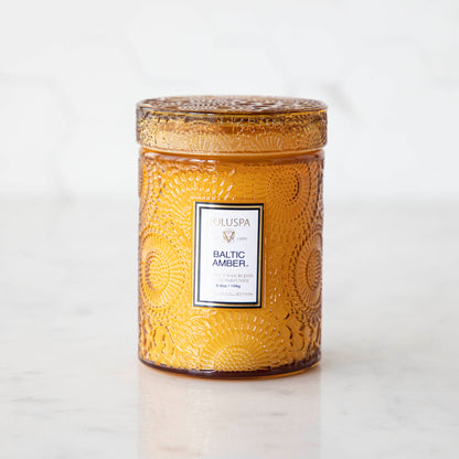Two Voluspa Baltic Amber candles with matches on a marble surface.