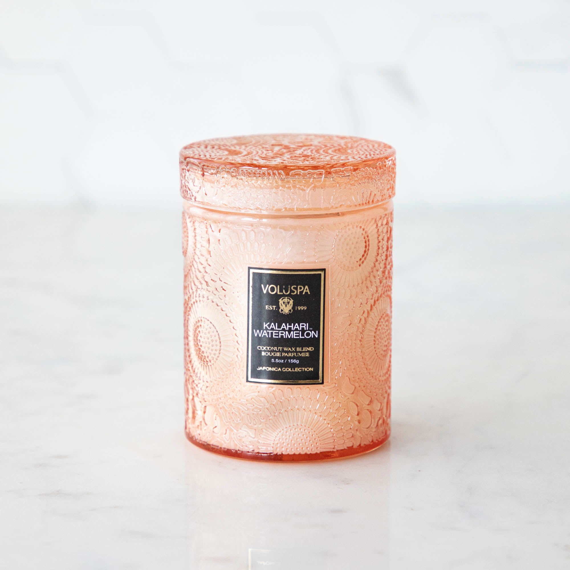 Two Voluspa Kalahari Watermelon candles on a marble surface with matches nearby, featuring a crisp cucumber aroma.