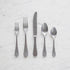 A set of Mepra Michelangelo Vintage 5-Piece Place Setting stainless steel flatware, including two forks, a knife, and two spoons, arranged in a line on a marble surface.