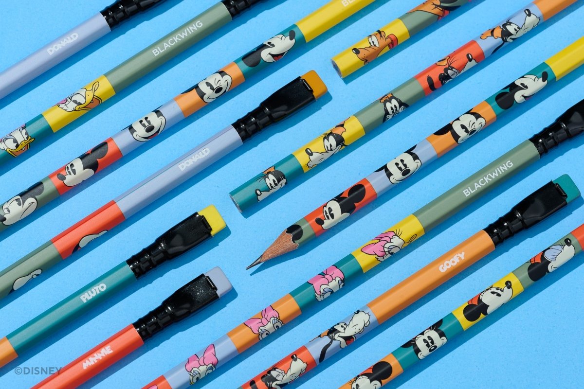 A set of colorful Disney-branded mechanical pencils arranged diagonally on a bright blue background. The pencils feature cartoon character prints including Mickey Mouse, Minnie Mouse, Pluto, and Goofy, with black erasers and black end caps.