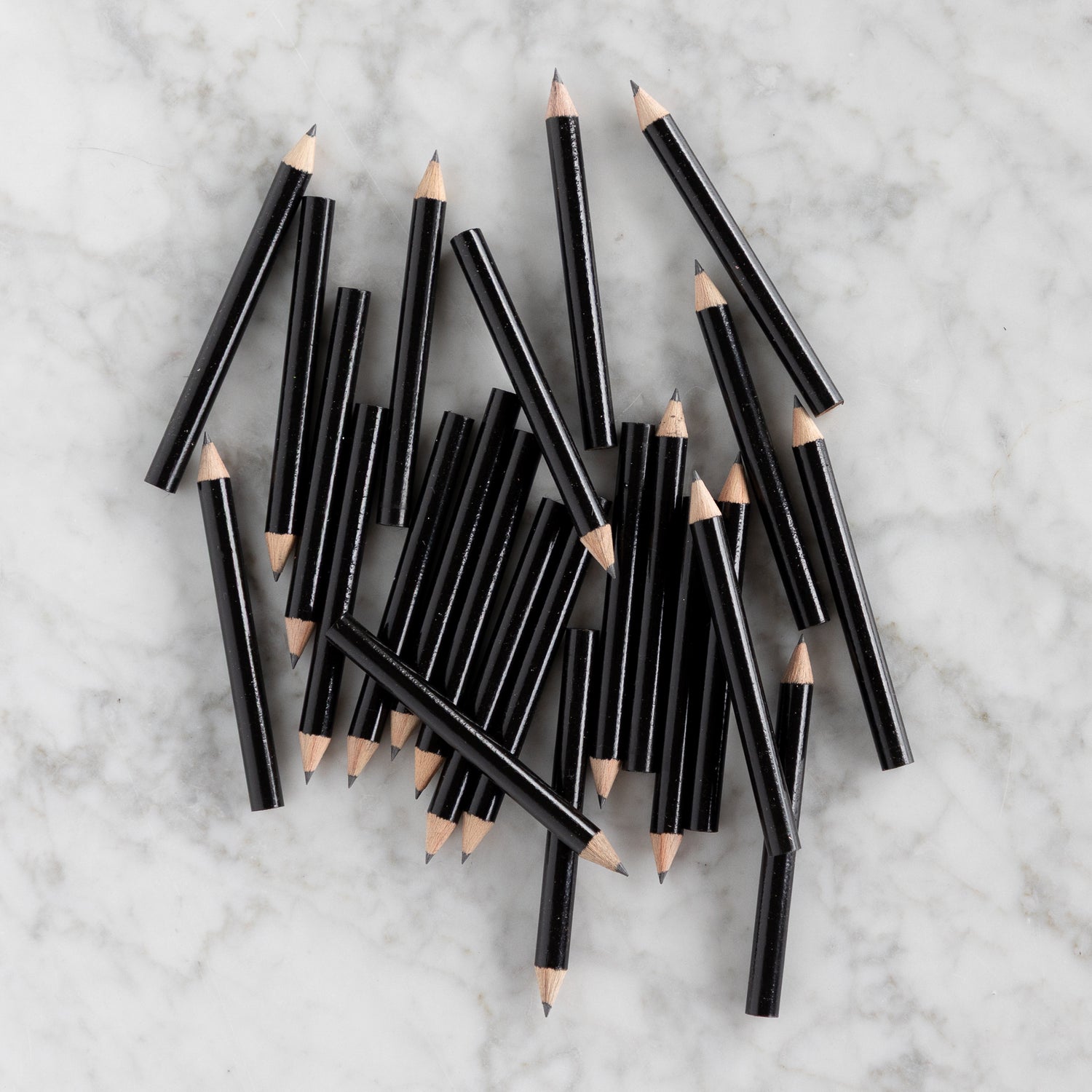 Mini Black Round Golf Pencils piled together on a marble background. 