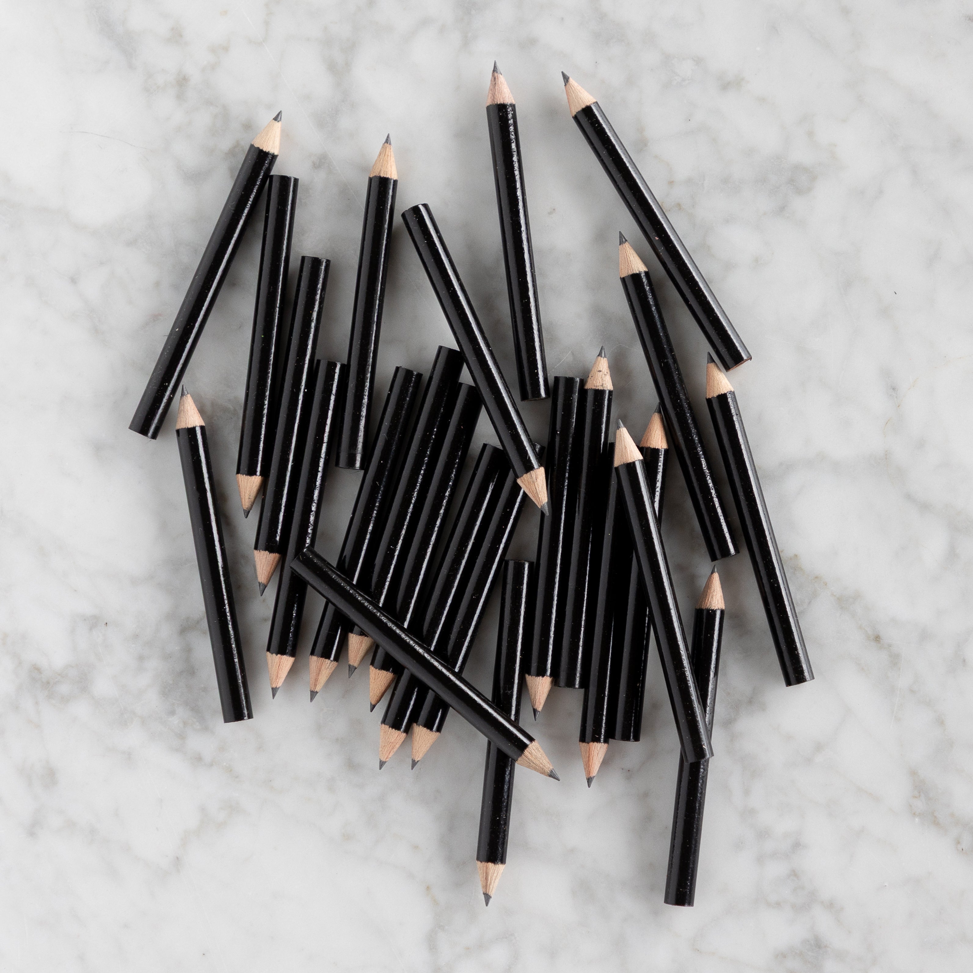 Mini Black Round Golf Pencils piled together on a marble background. 
