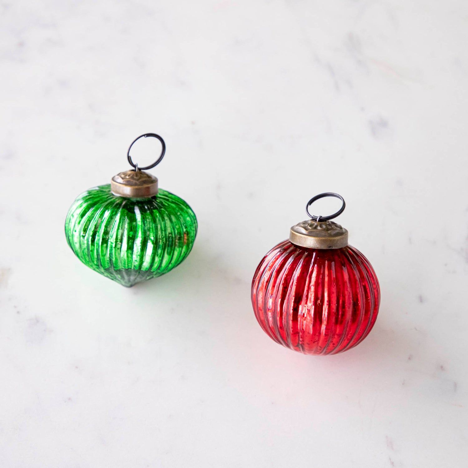 Mini green and red ribbed ornaments on a marble table.