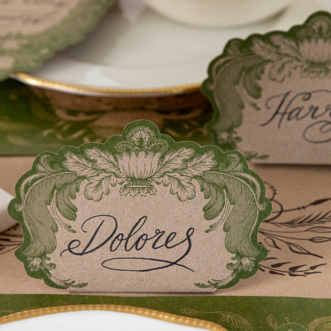 Close-up of a Moss Fable Toile Place Card labeled &quot;Dolores&quot; standing behind the plate of an elegant place setting.