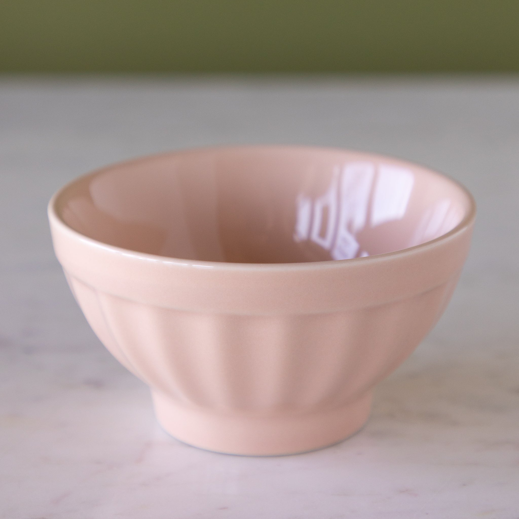 Blush-pink colored ceramic ice cream bowl on a marble table.