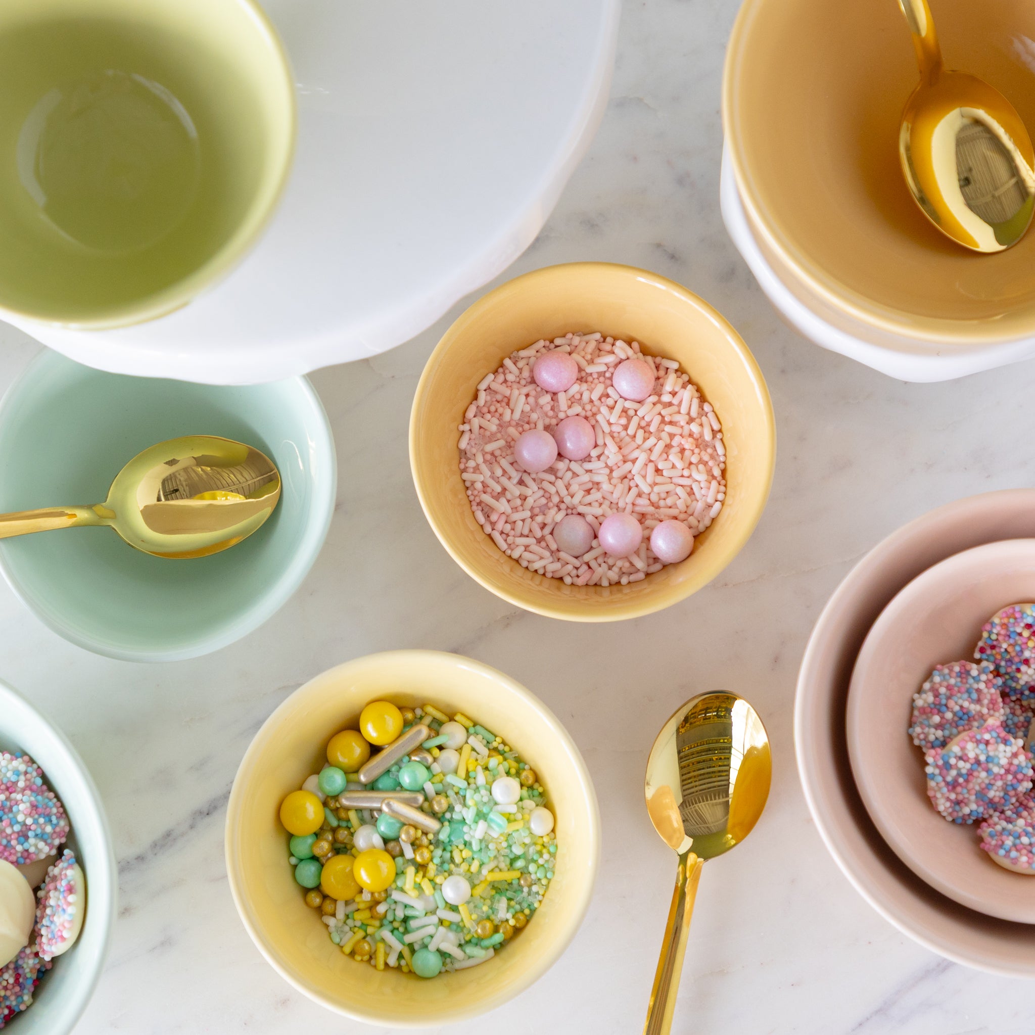 Colorful Sorbet Bowls with decorative sprinkles and gold spoons on a marble surface.