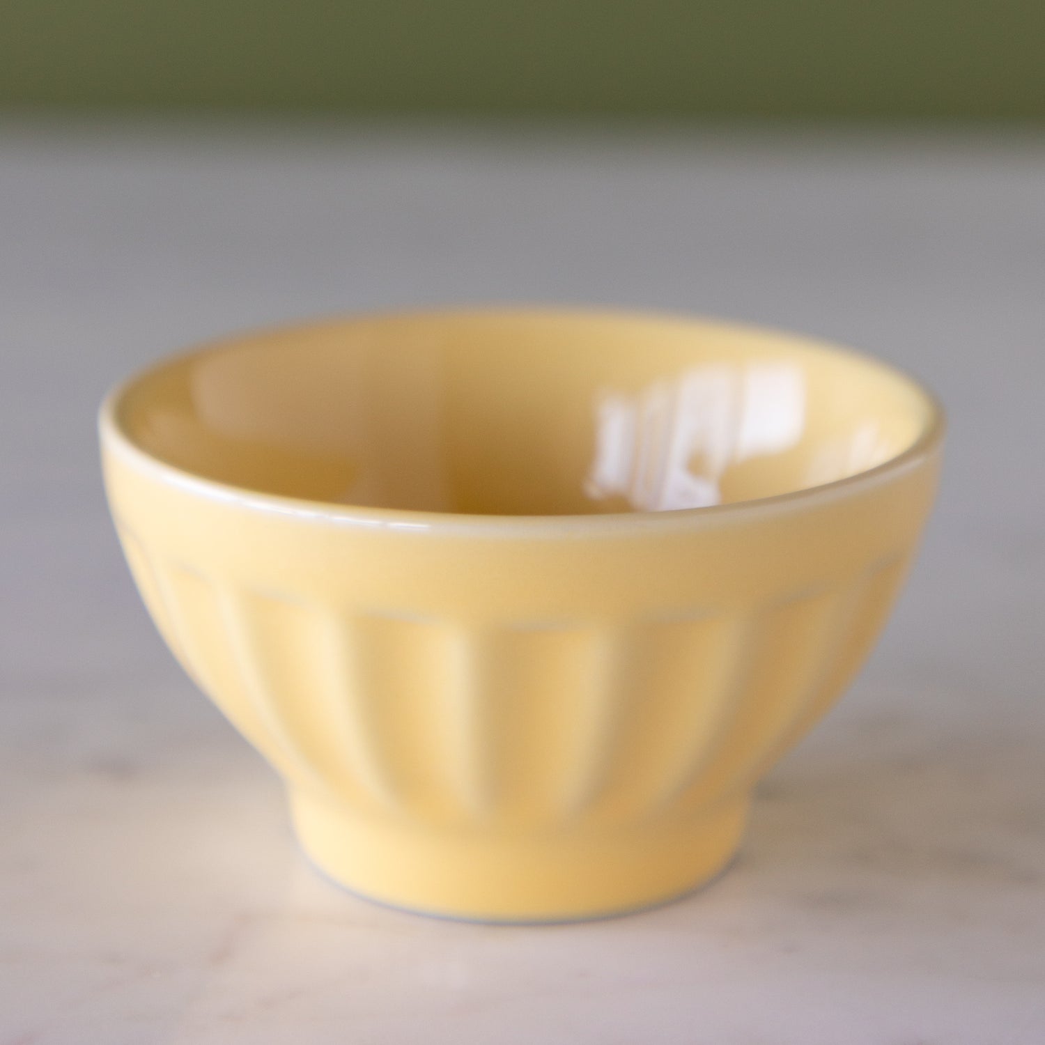 Butter-cream yellow colored ceramic pinch bowl on a marble table.
