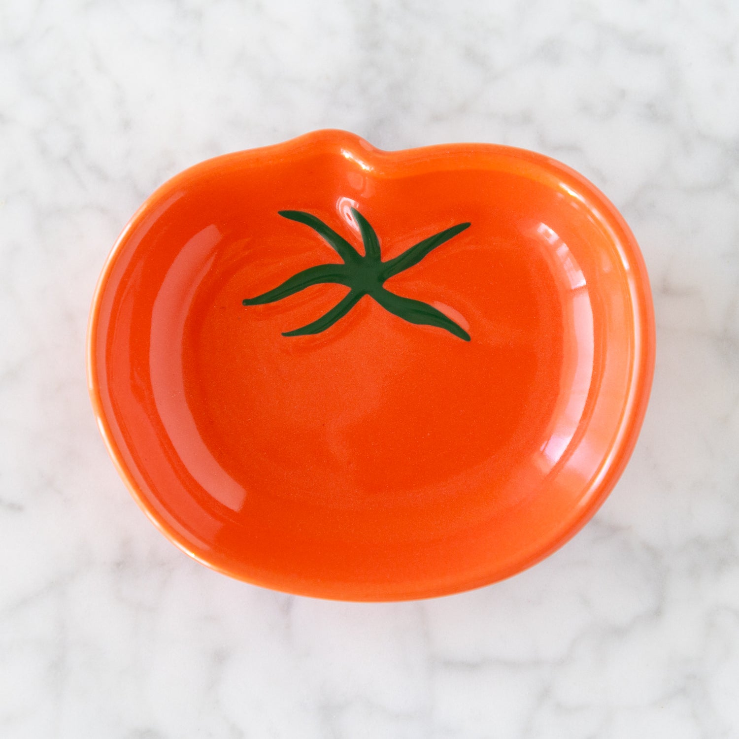 Orange ceramic dish shaped like a tomato with green stem on a white textured background.