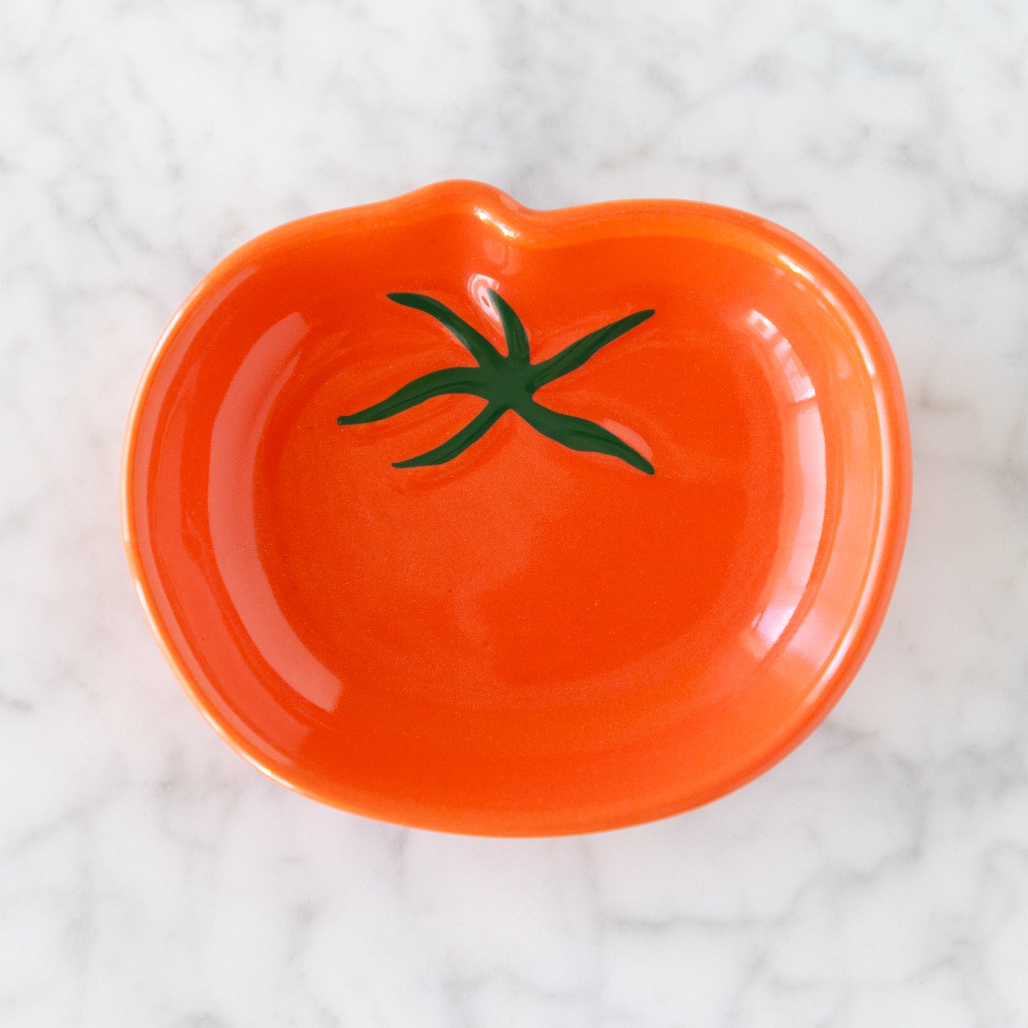 Orange ceramic dish shaped like a tomato with green stem on a white textured background.