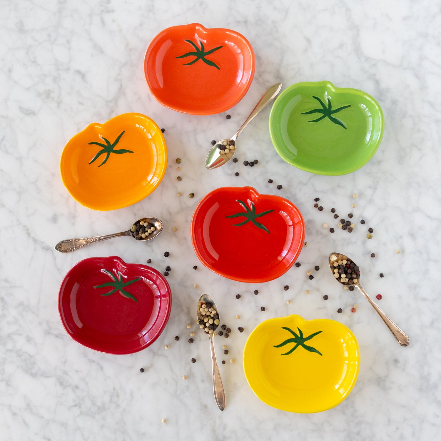 Set of colorful tomato-shaped bowls with spoons on a marble surface.