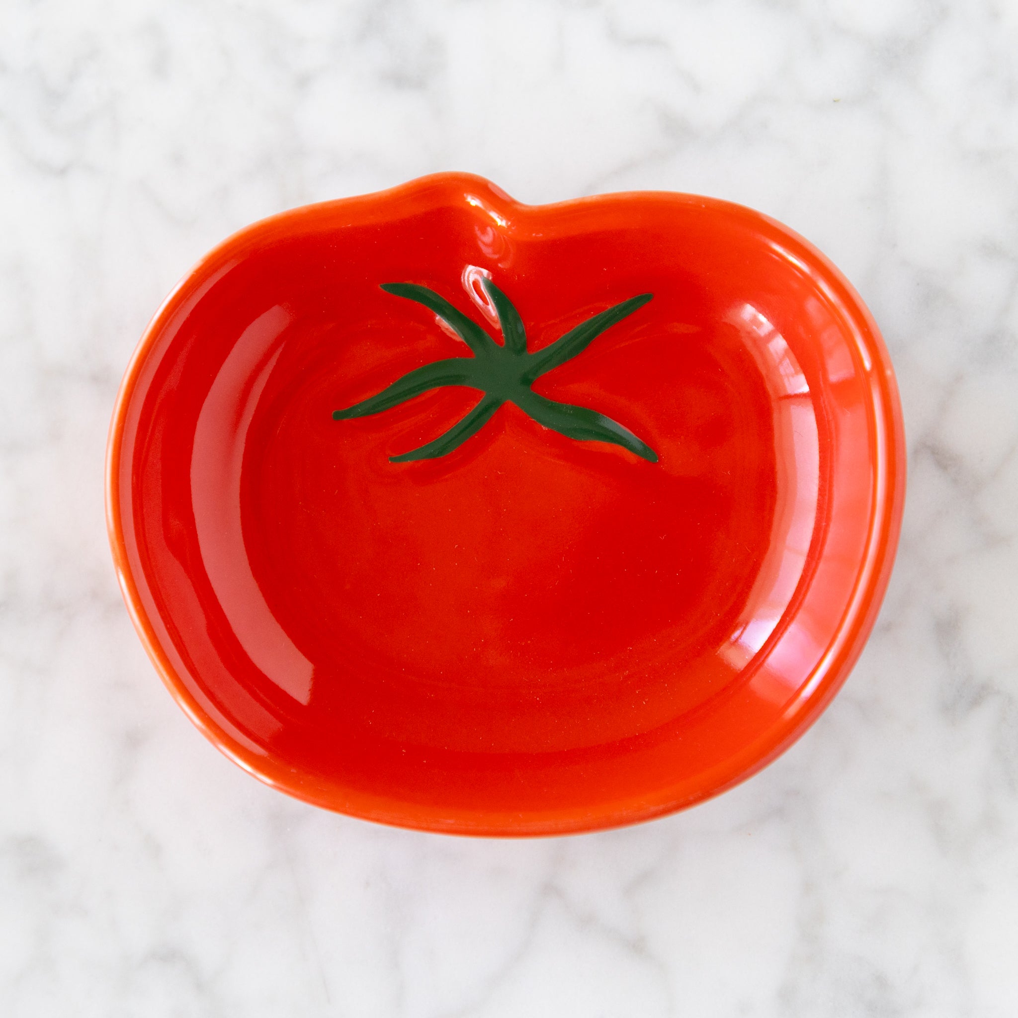 Red tomato-shaped plate with green stem on a white textured background.