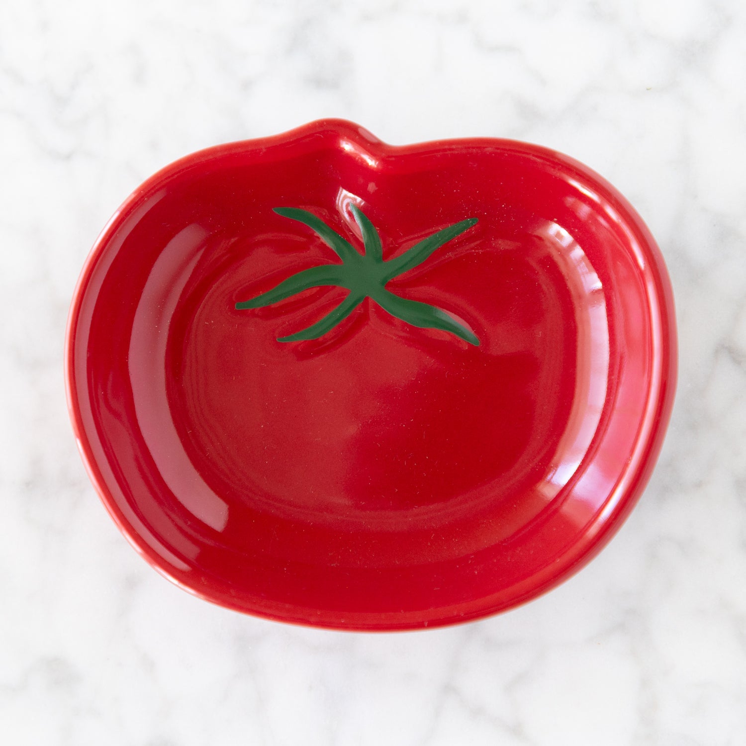 Red tomato-shaped dish with a green stem on a white marble surface.