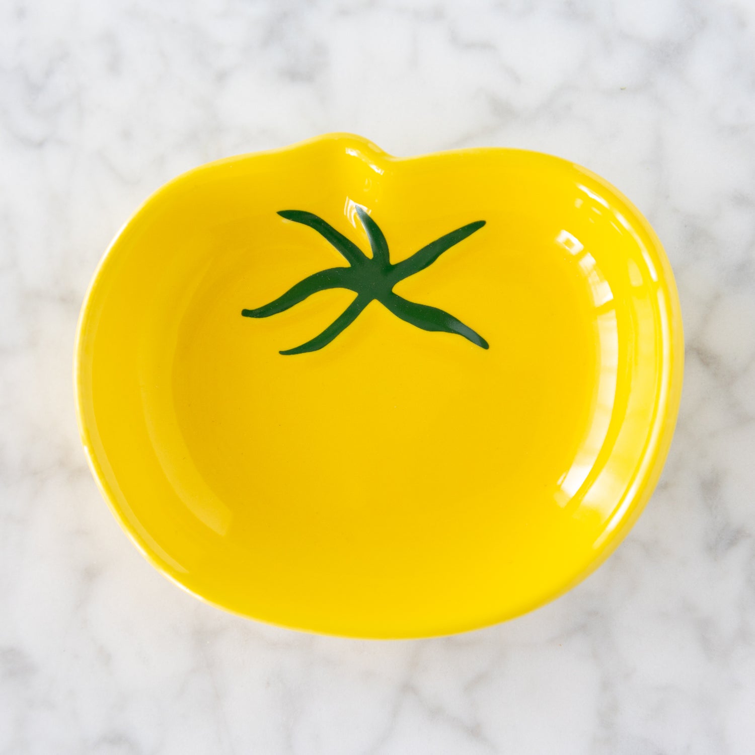 Yellow tomato shaped ceramic pinch bowl with green stem design on a white marble surface.