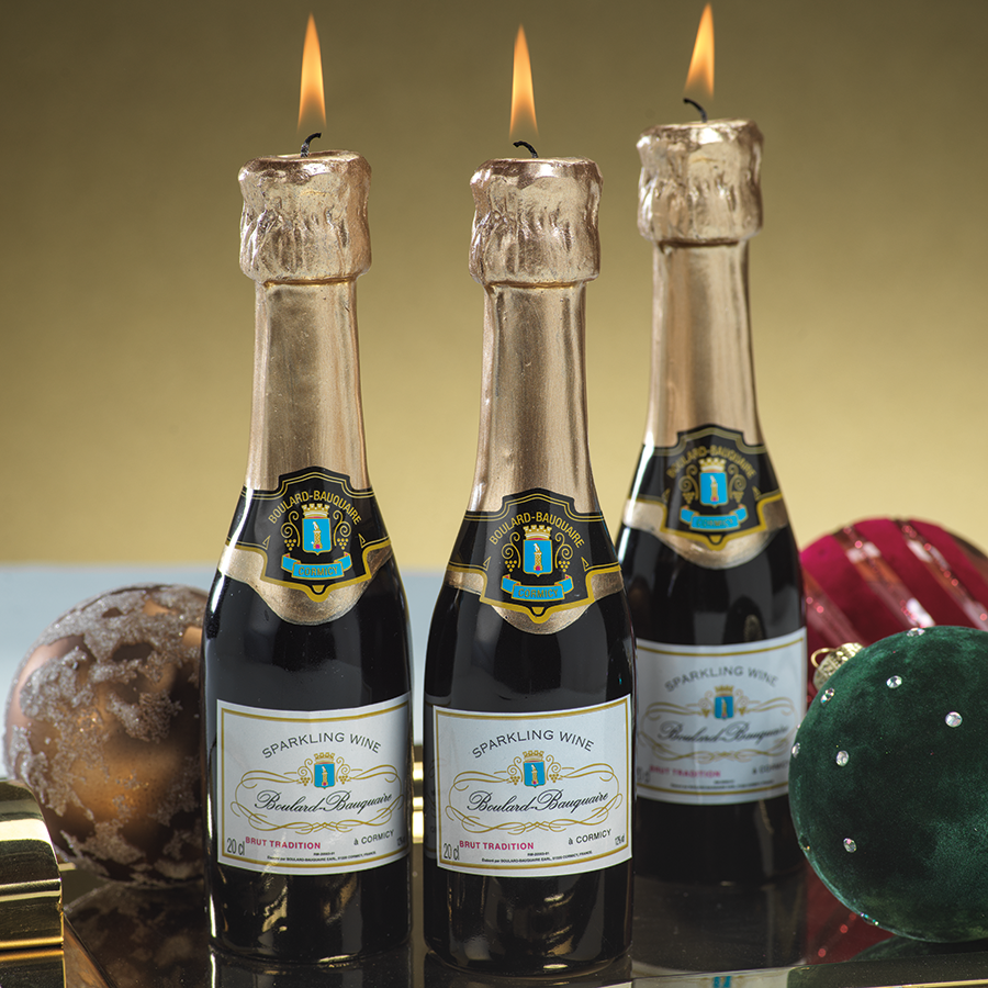 Three Zodax Mini Champagne Bottle Candles with lit candles on top, set against a celebratory backdrop as part of an elegant event table setting.