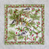 A square white fabric napkin with a detailed winter woodland print featuring birds, pine branches, pinecones, and red berries, folded and stacked on a light gray marble surface.