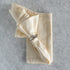 Folded beige napkin with a silver napkin ring on a gray textured surface.