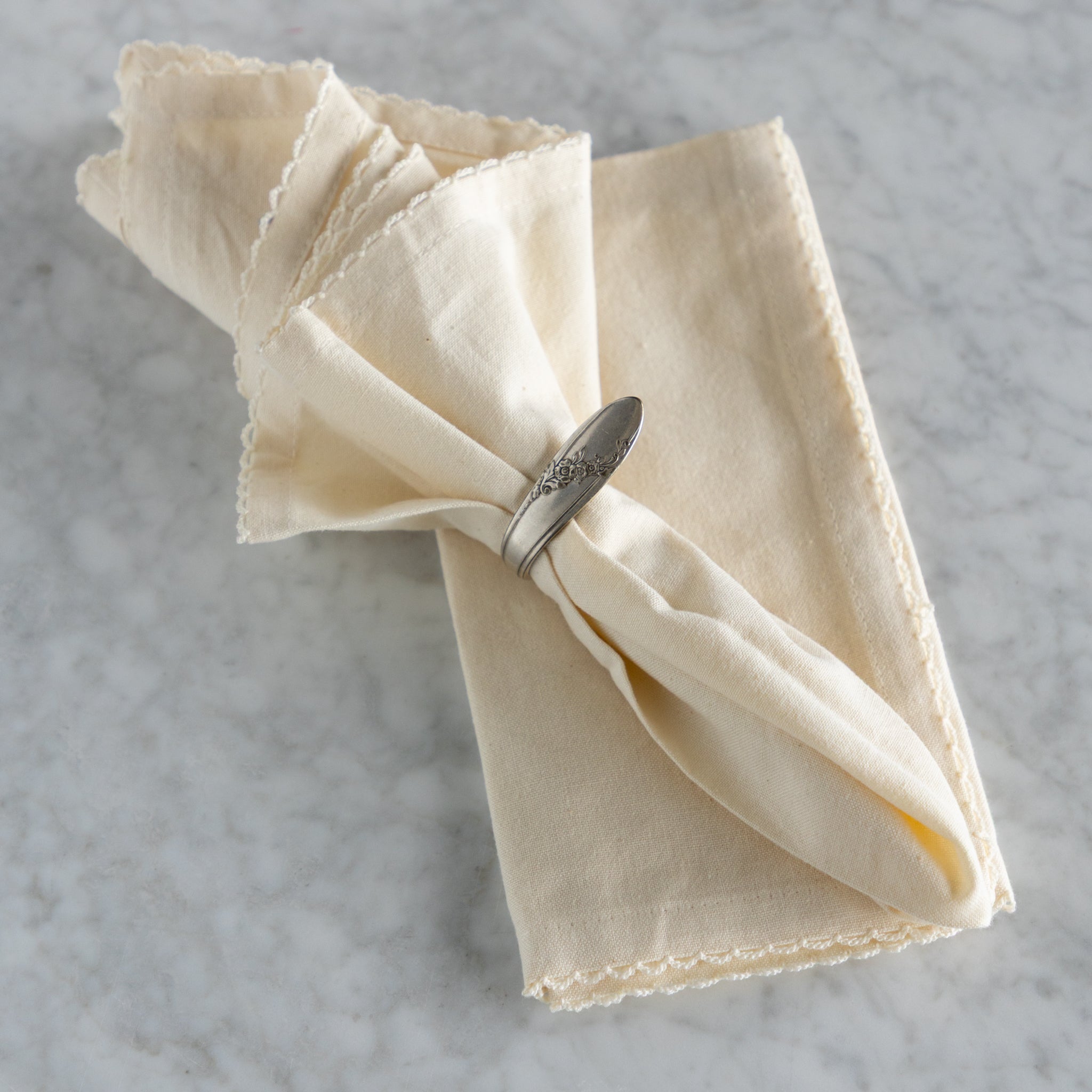 Folded beige napkin with a silver napkin ring on a gray textured surface.