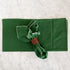 A dark green fabric napkin with white embroidered trim, gathered and secured with a brown leather napkin ring on a light gray marble surface.