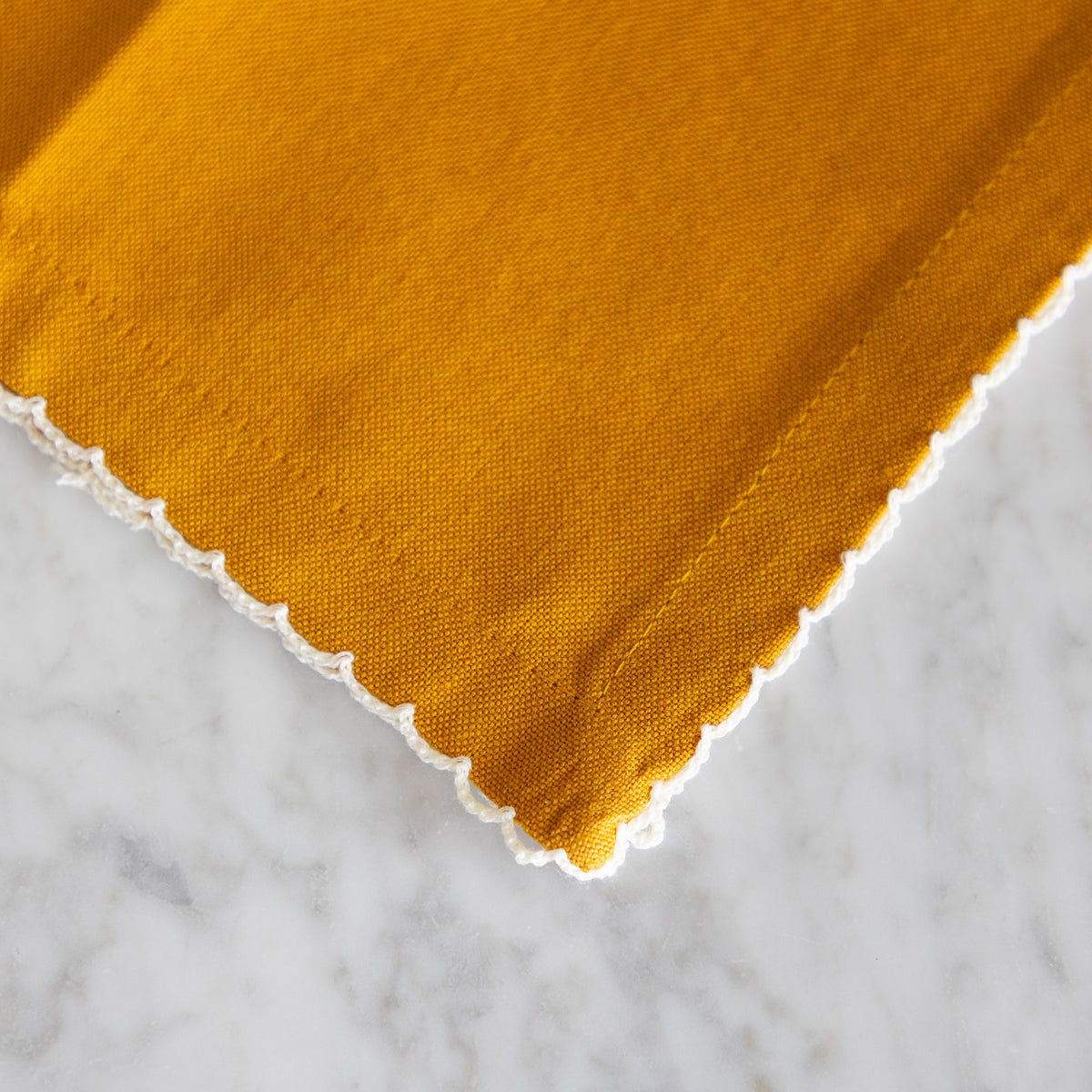 Close up detail of the white lace trim on a mustard colored cotton napkin. 