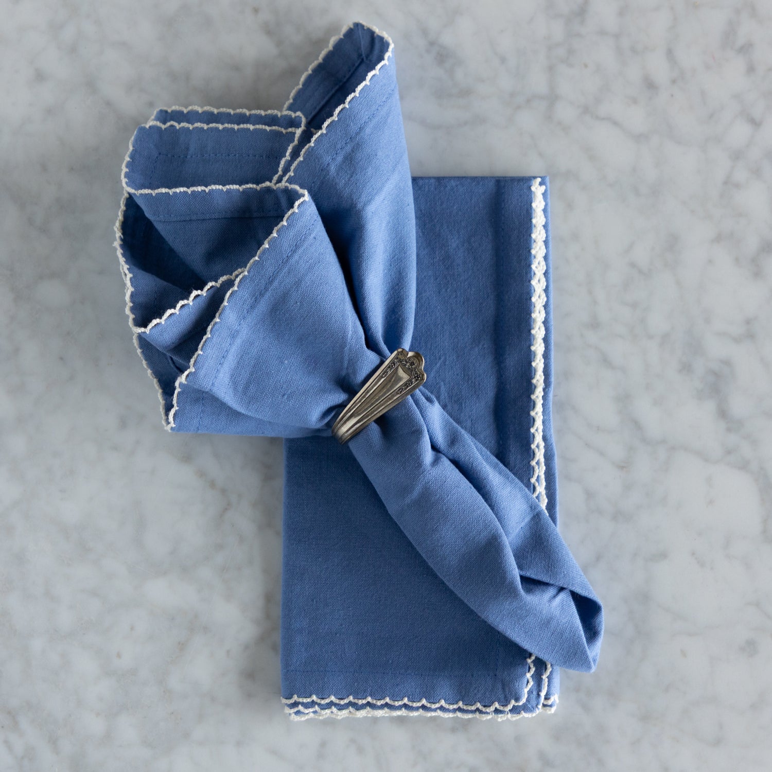 Folded blue napkin with a decorative clip on a gray surface.