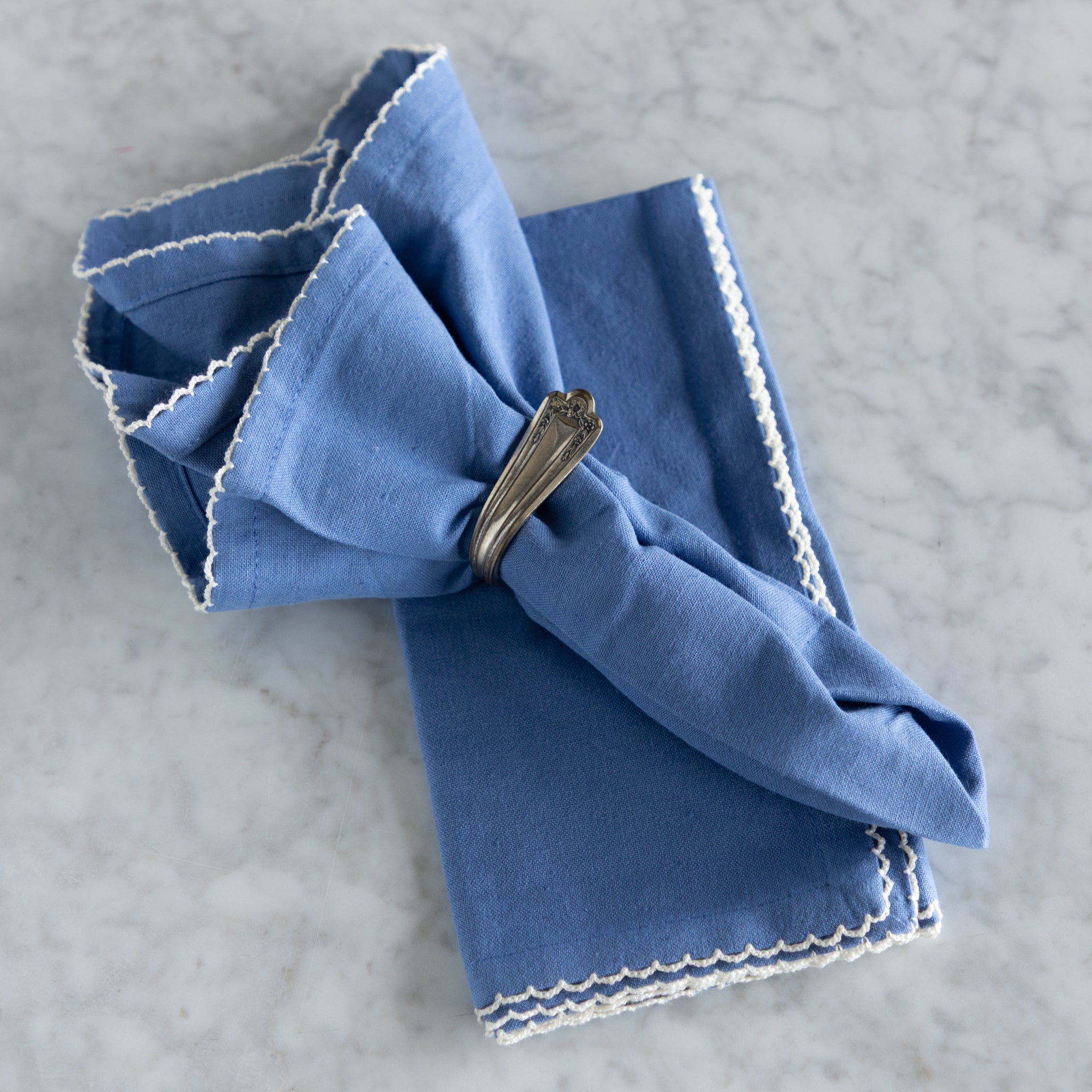 Folded blue napkin with a decorative edge on a gray surface.