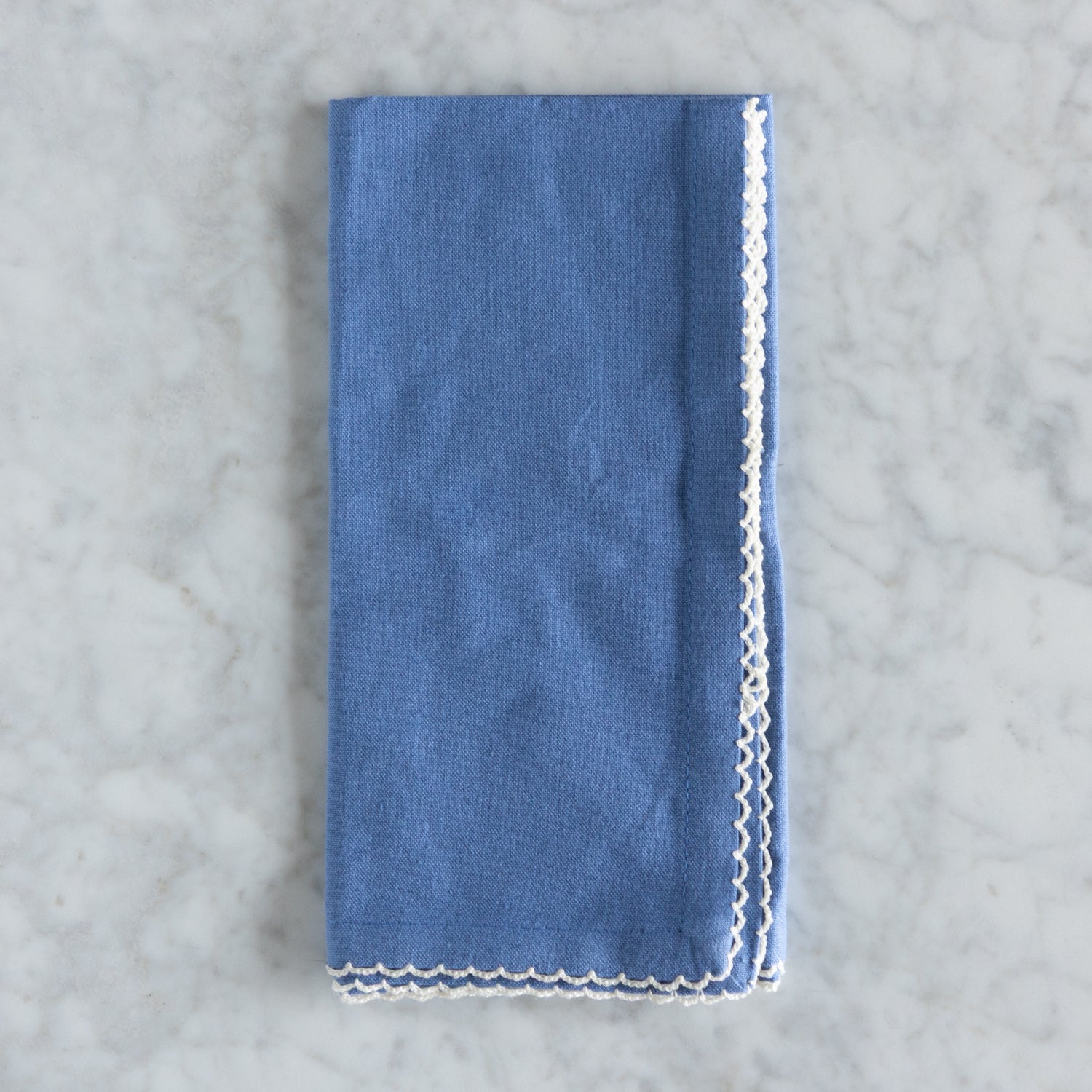 Blue napkin with white lace trim on a gray marble background.
