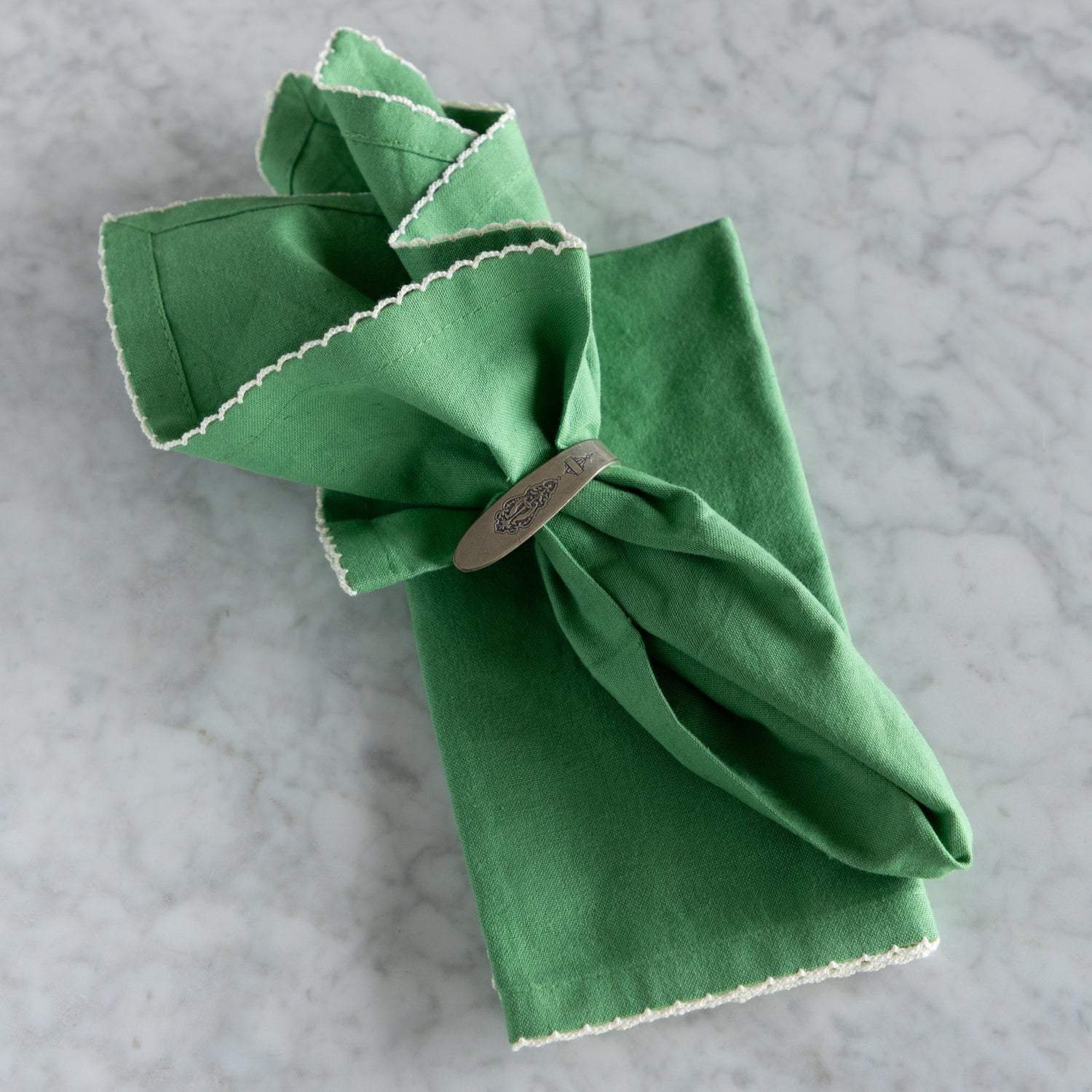 Green folded napkin with a silver napkin ring on a gray surface.
