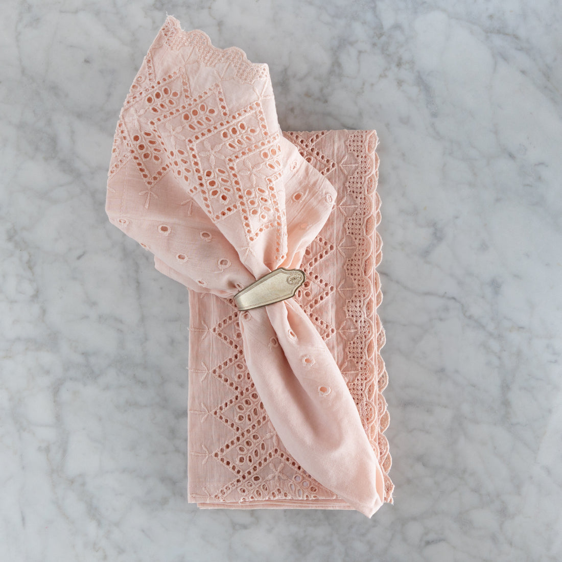 Pink lace napkin with a silver napkin ring on a marble surface.