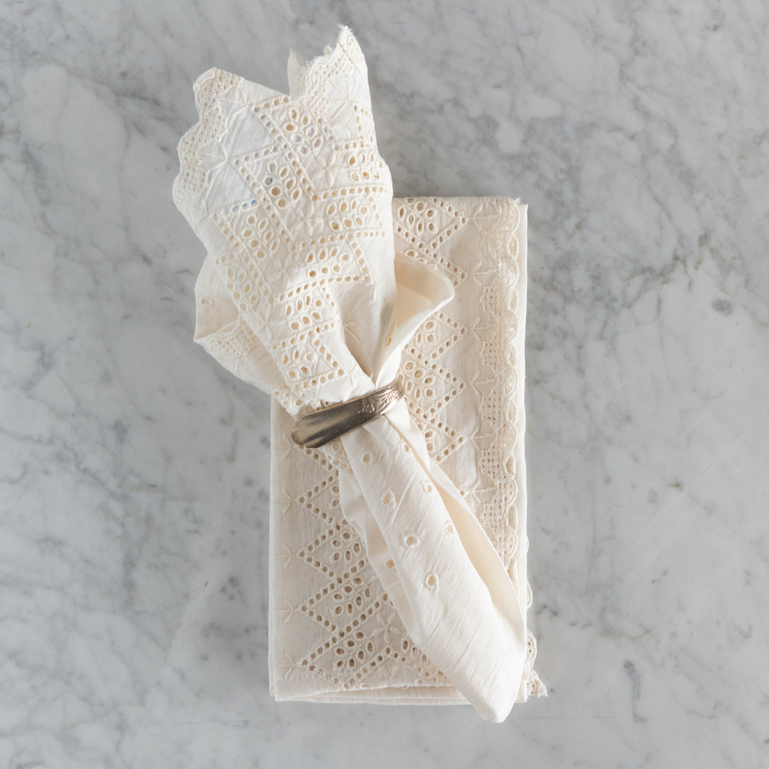 White lace napkin folded and tied with a silver napkin ring on a marble surface.