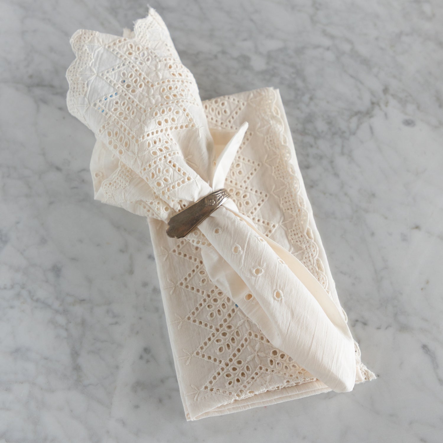 White lace napkin with a silver napkin ring on a marble surface.