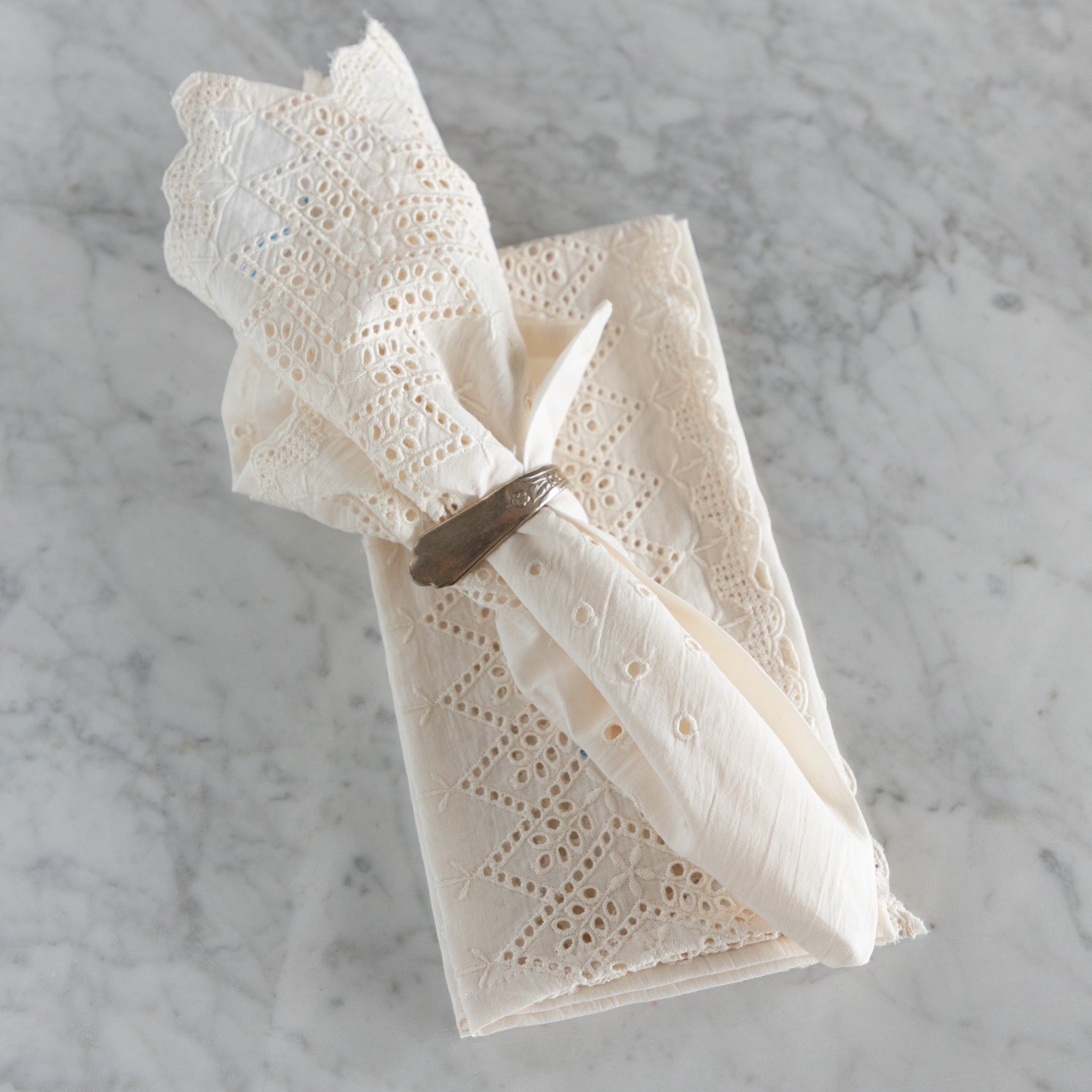 White lace napkin with a silver napkin ring on a marble surface.