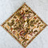 Cloth napkin with Fall colors and motif printed on it laying flat on a marble surface with another napkin held by a leather strap laying on top of it. 
