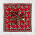 A square red cloth napkin with a green holly and berry border pattern, laying flat on a marble surface and tied with a shiny olive-green ribbon.