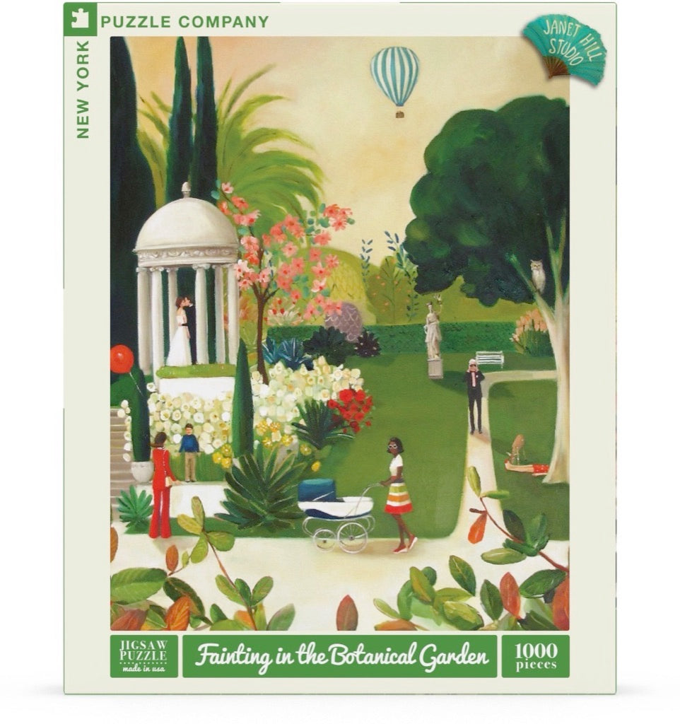 A New York Puzzle Company jigsaw puzzle box featuring an illustration by artist Janet Hill of a serene botanical garden scene with a hot air balloon in the sky.