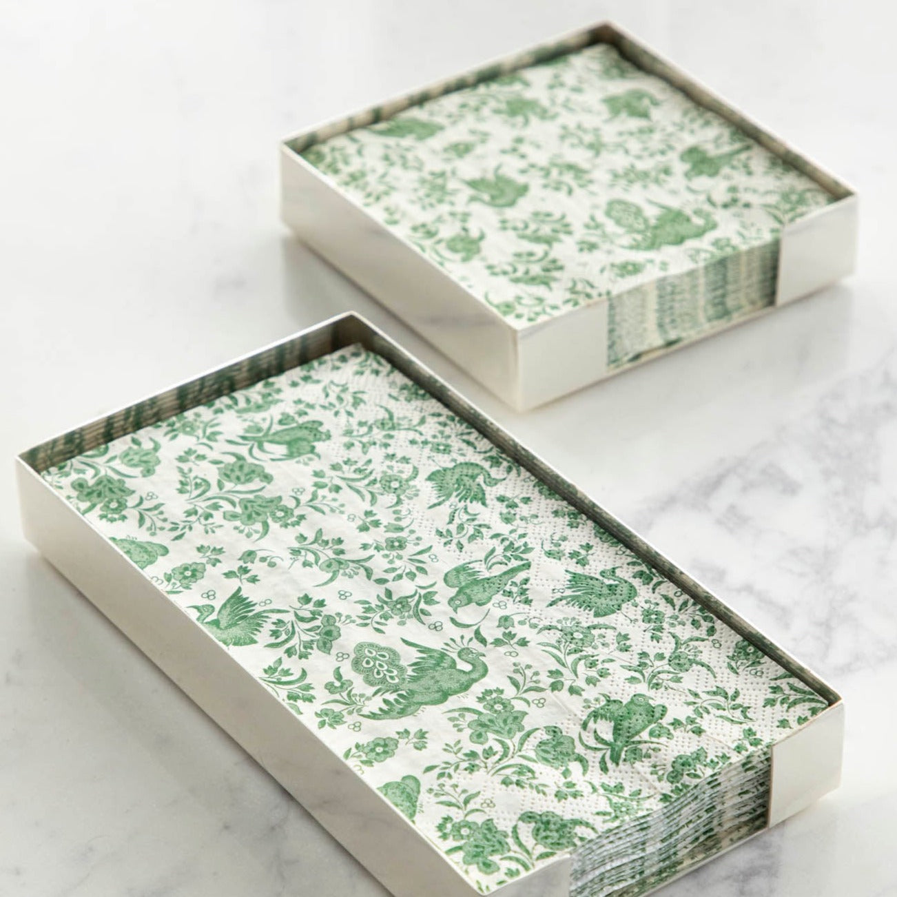 Two Silver Napkin Holders, guest-sized and cocktail-sized, containing green and white napkins on a white table.