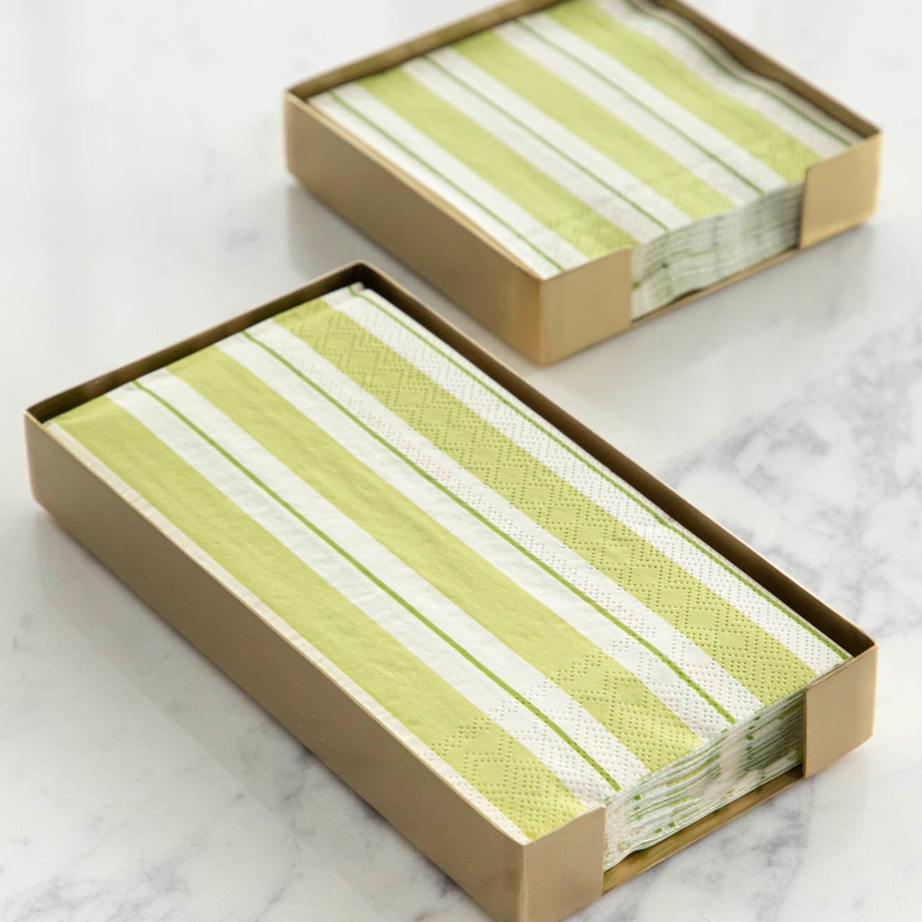 Two Brass Napkin Holders, guest-sized and cocktail-sized, containing green striped napkins on a white table.