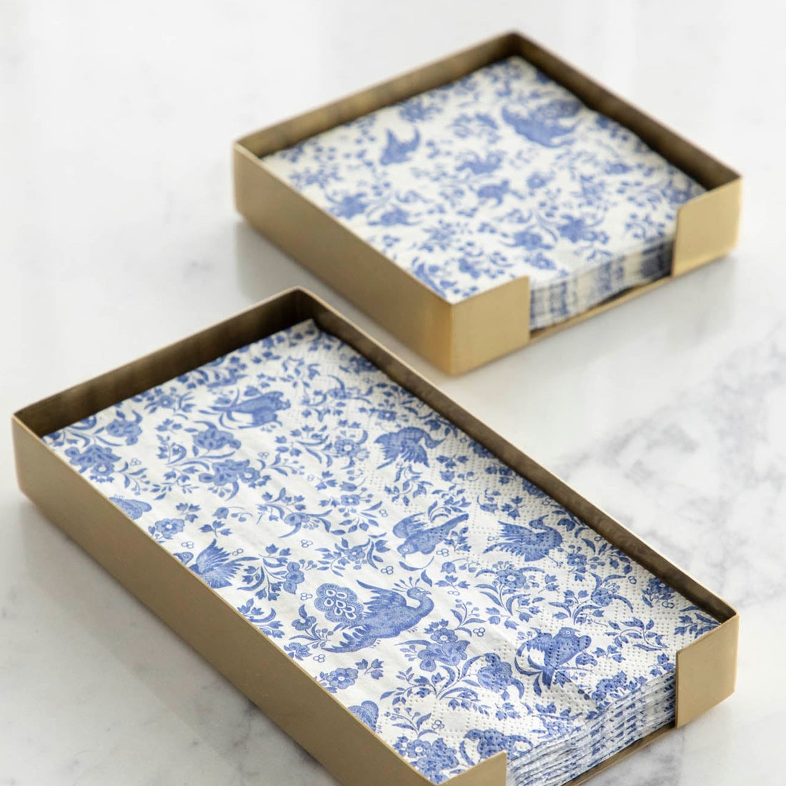 Two Brass Napkin Holders, guest-sized and cocktail-sized, containing blue and white napkins on a white table.