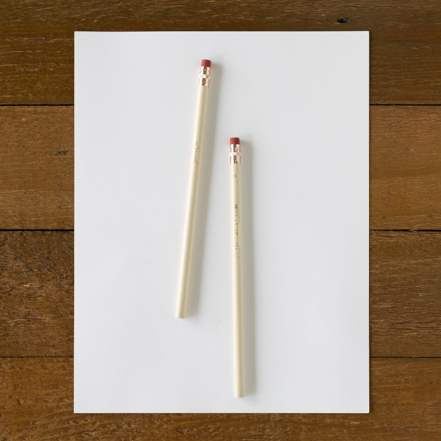 Two pencils on a white sheet of paper with a wooden surface background.