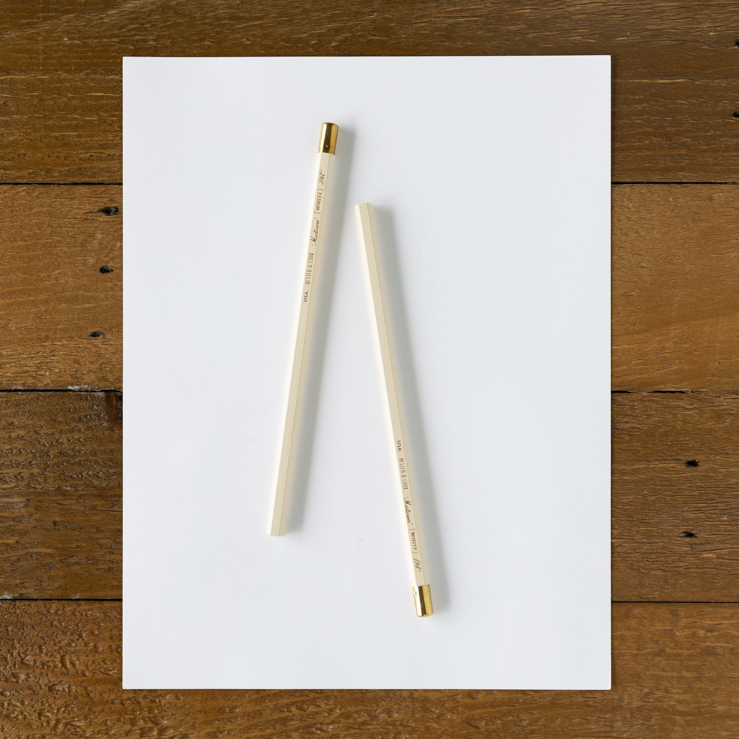 Two pencils on a white sheet of paper with a wooden surface background.