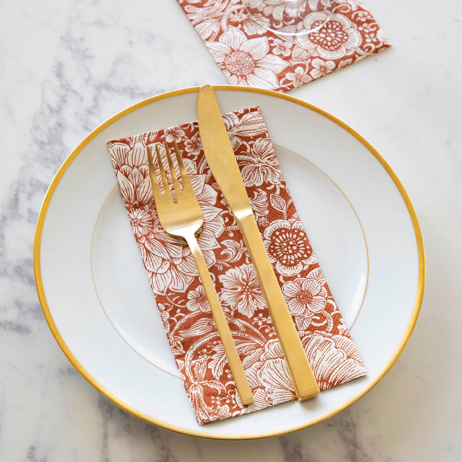 A Harvest Bouquet Guest Napkin centered on a gold-rimmed white plate with gold cutlery on top.