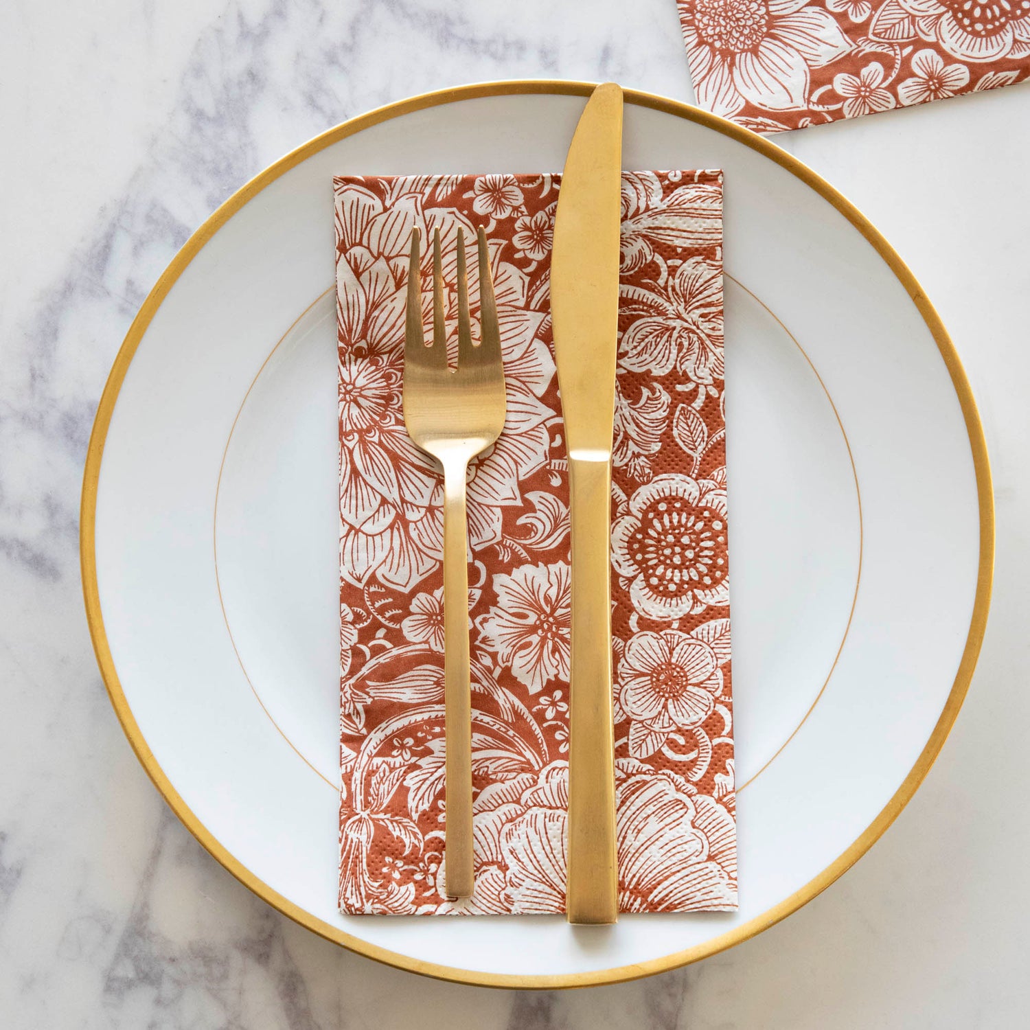 A Harvest Bouquet Guest Napkin centered on a gold-rimmed white plate with gold cutlery on top, from above.
