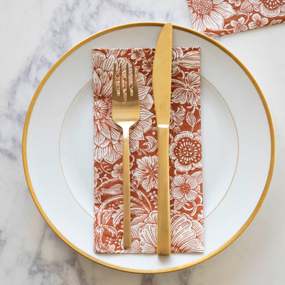 A Harvest Bouquet Guest Napkin centered on a gold-rimmed white plate with gold cutlery on top, from above.