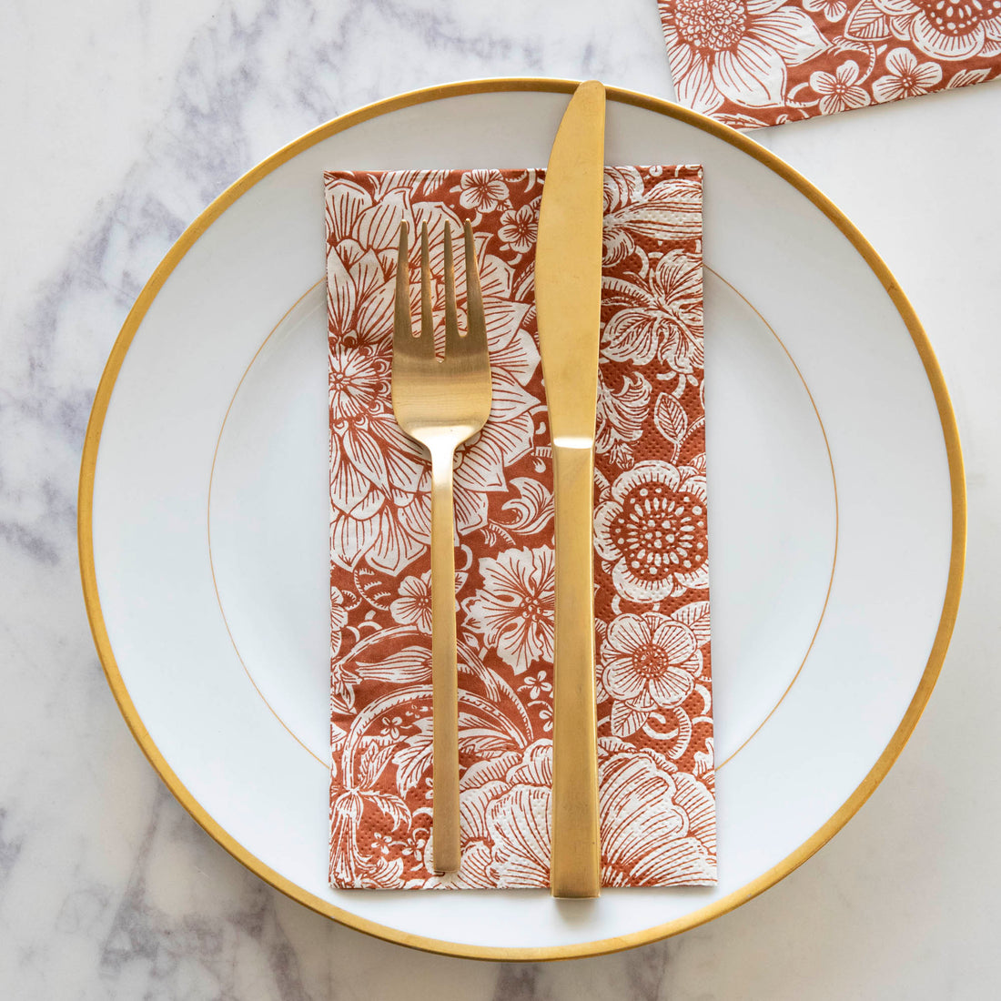 A Harvest Bouquet Guest Napkin centered on a gold-rimmed white plate with gold cutlery on top, from above.