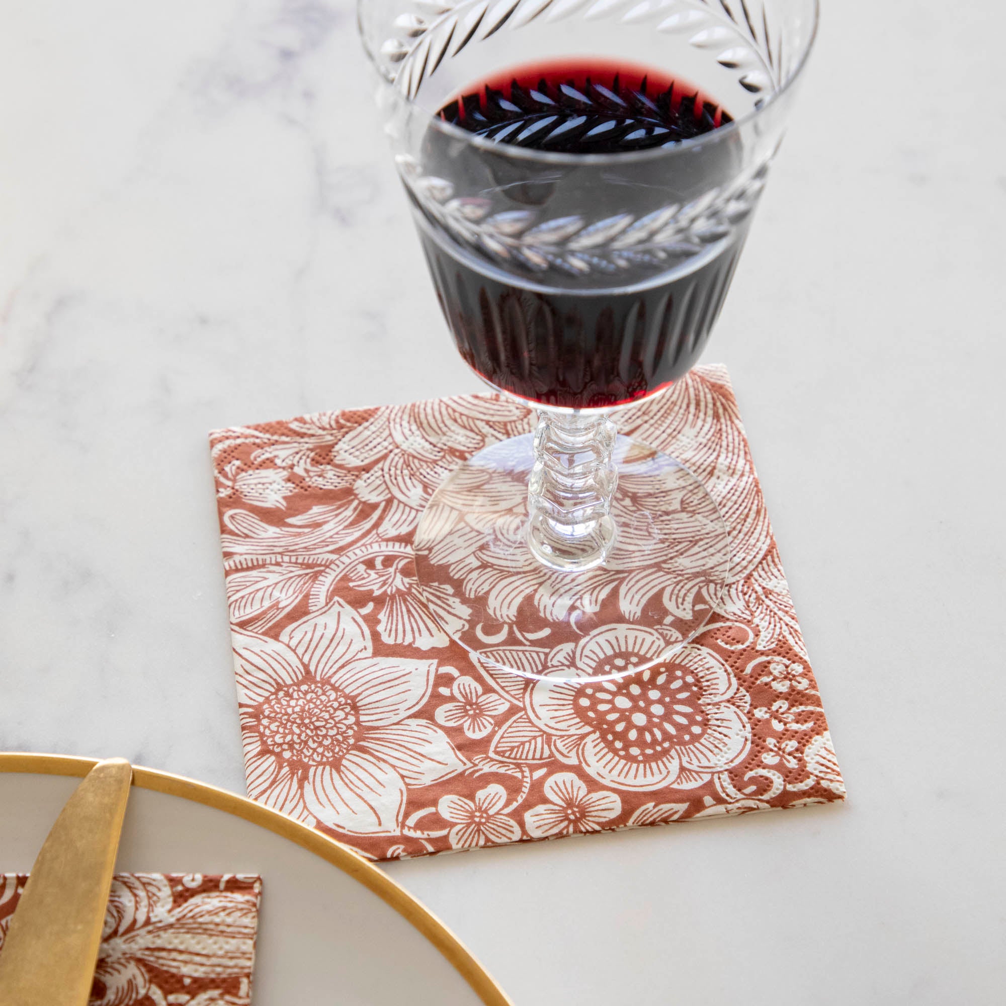 A Harvest Bouquet Cocktail Napkin under a glass of red wine with an elegant place setting.