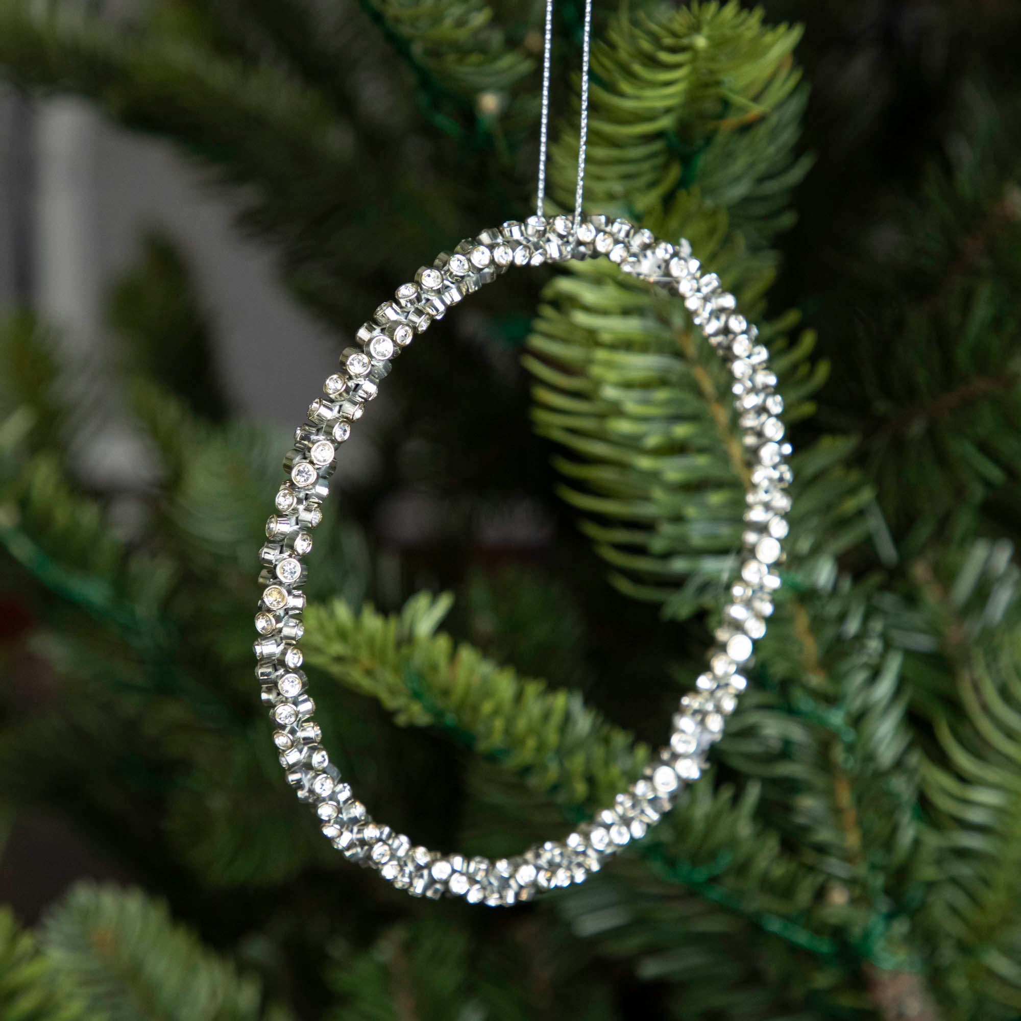 Silver Diamond Ring Ornament hanging on a tree by a silver string.