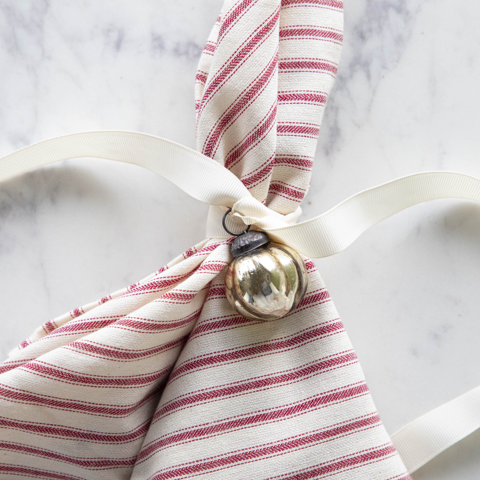 Embossed Antique Gold Mercury Glass Ornament tied to a red stripe napkin.
