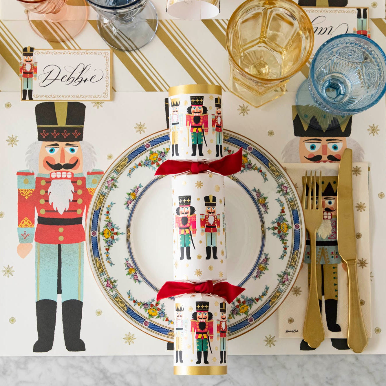 Christmas theme place setting with the Nutcrackers Placemat, vintage plate with the Nutcracker Festive Cracker atop, colorful glassware and Nutcracker Place Card on the Gold Peppermint Stripe Runner.